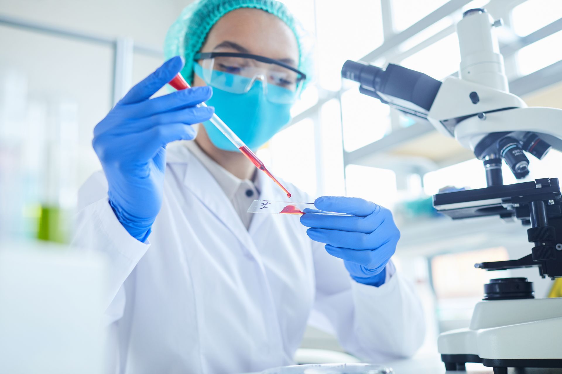 A female scientist is holding a test tube in front of a microscope.