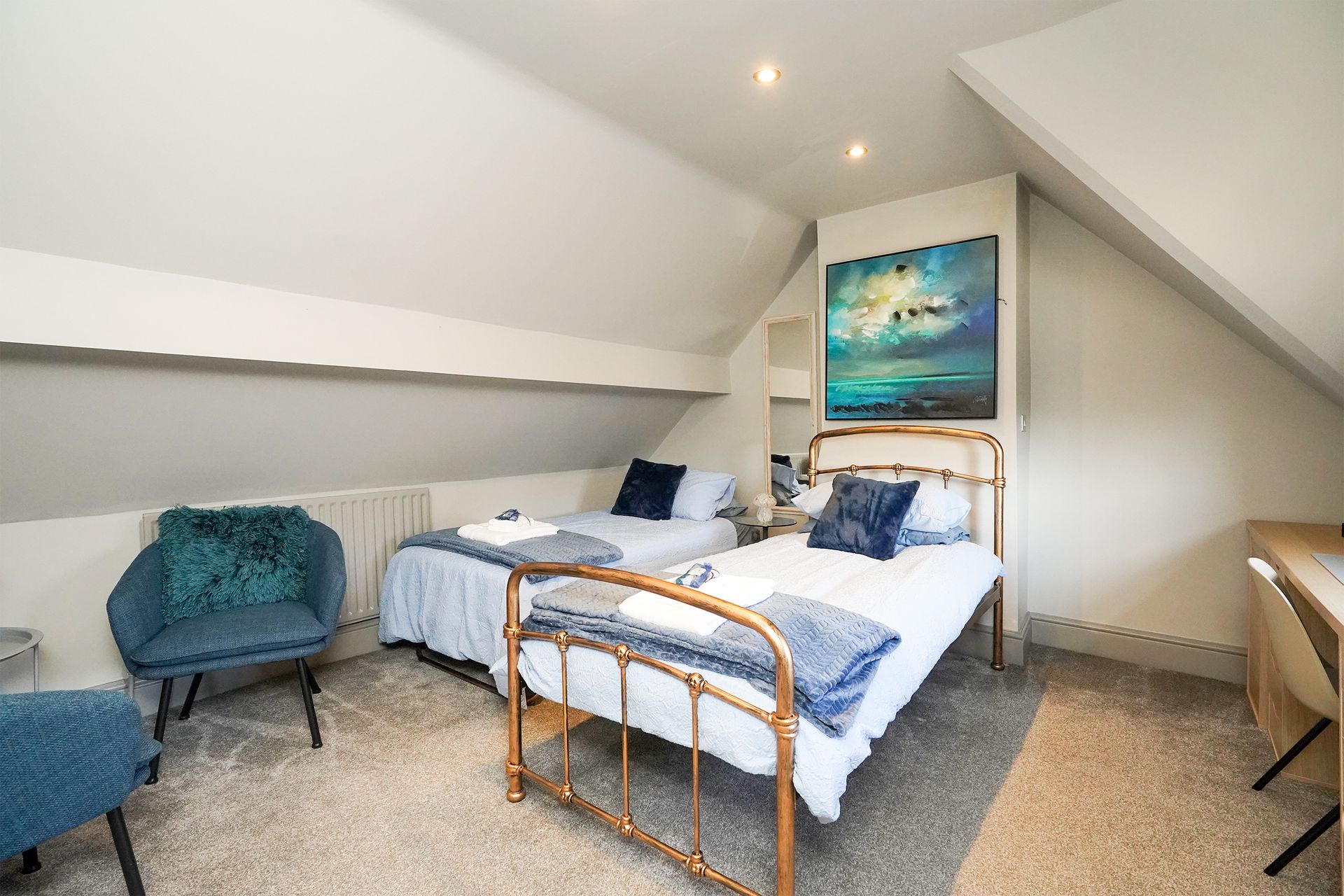 Attic bedroom with two single beds, teal chair, and sloped white ceiling.