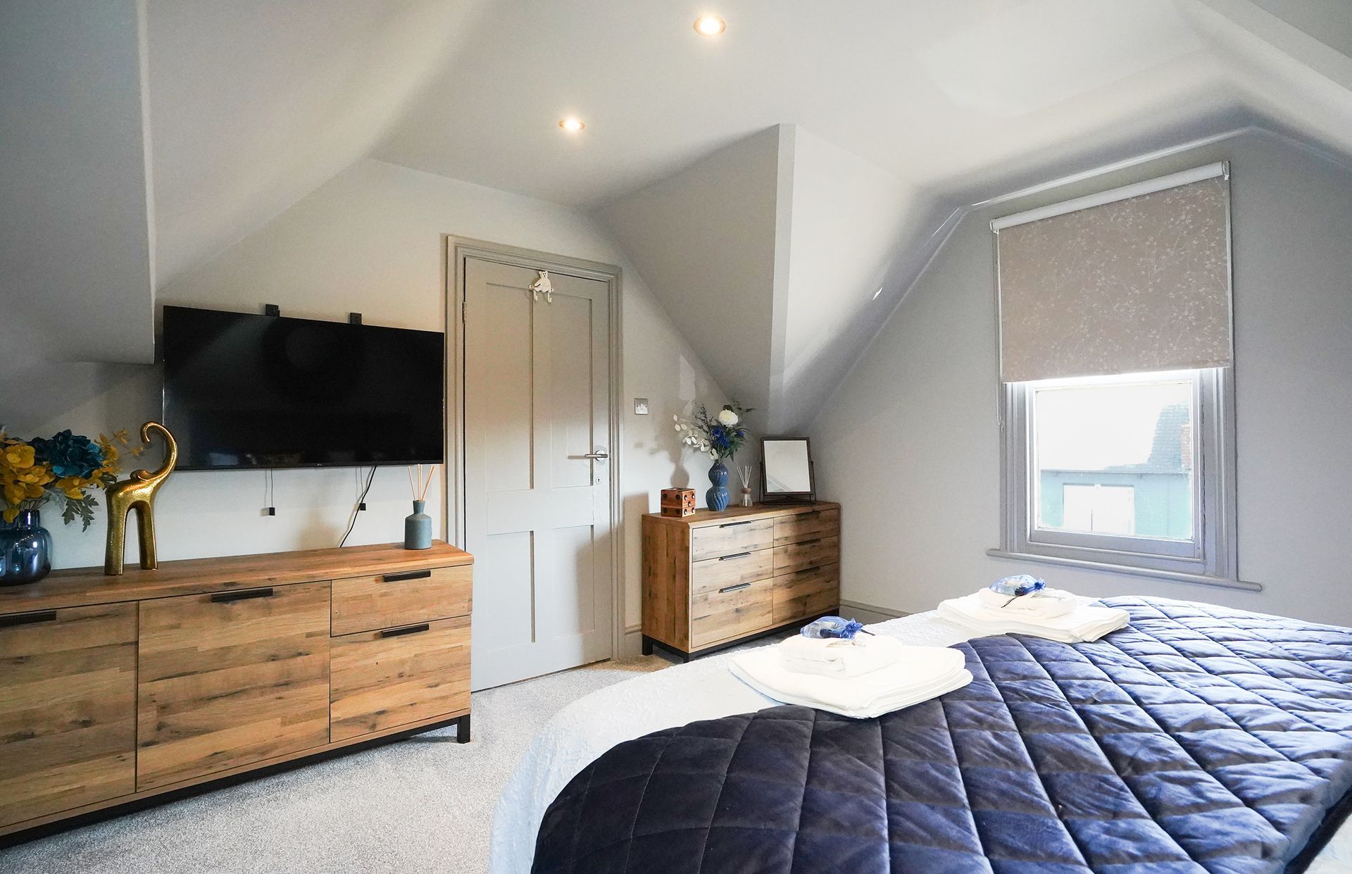 Bedroom with gray walls, TV, dresser, closet doors, and bed with dark blue quilt near a window with blinds