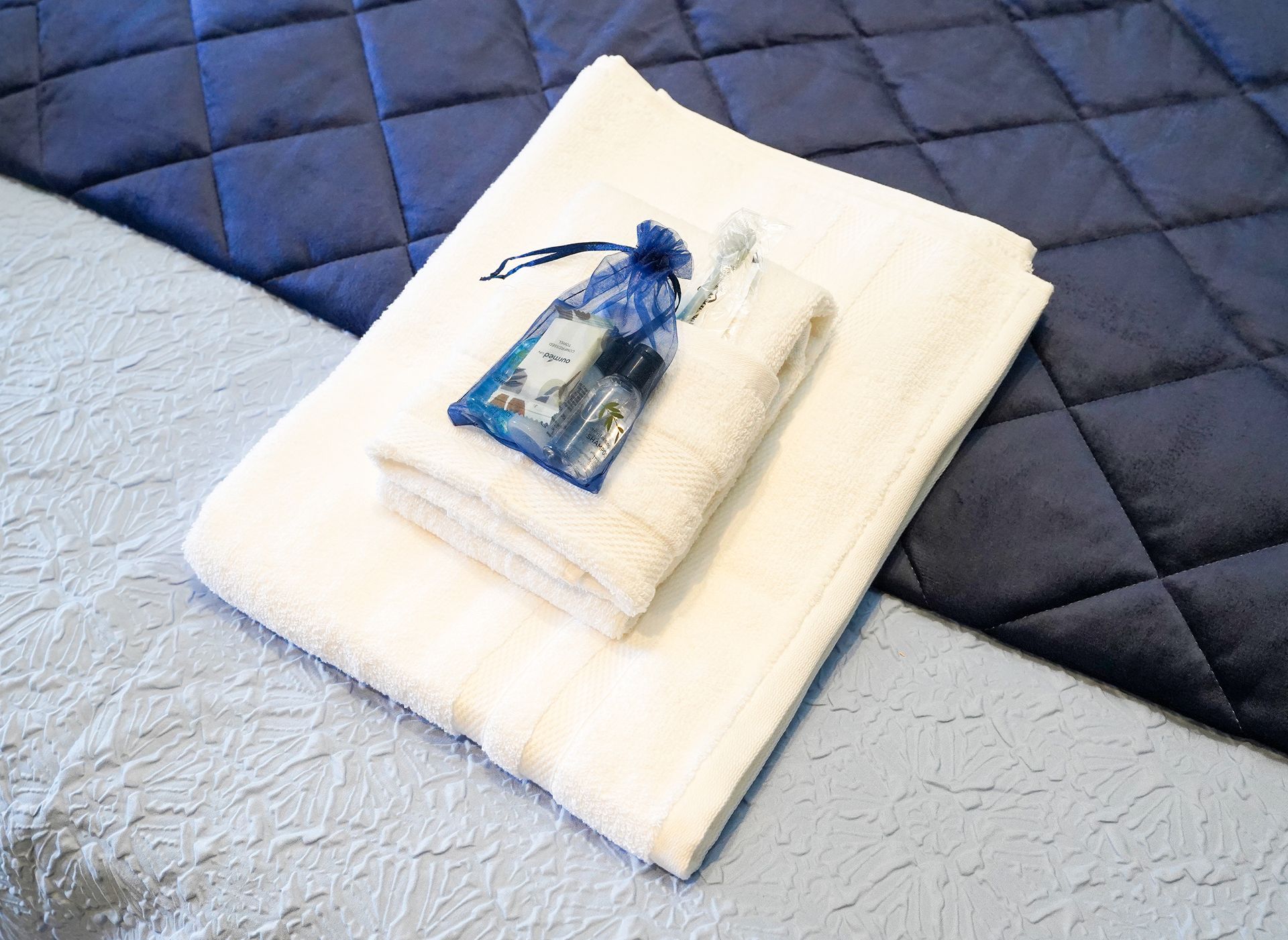 Folded white towels with a blue decorative bottle on a quilted navy and light blue bedspread