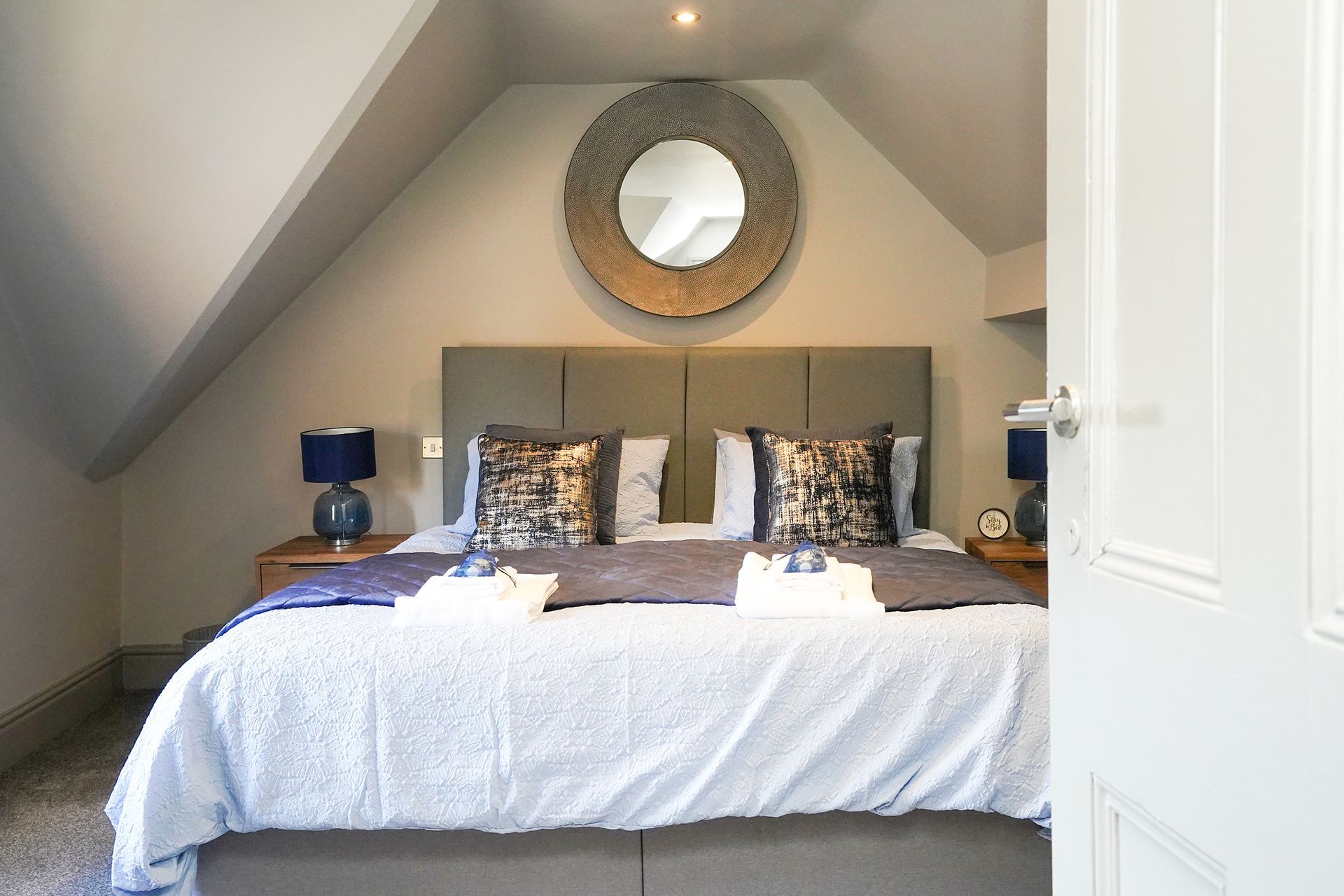 Cozy attic bedroom with a large bed, round mirror, and blue bedside lamps