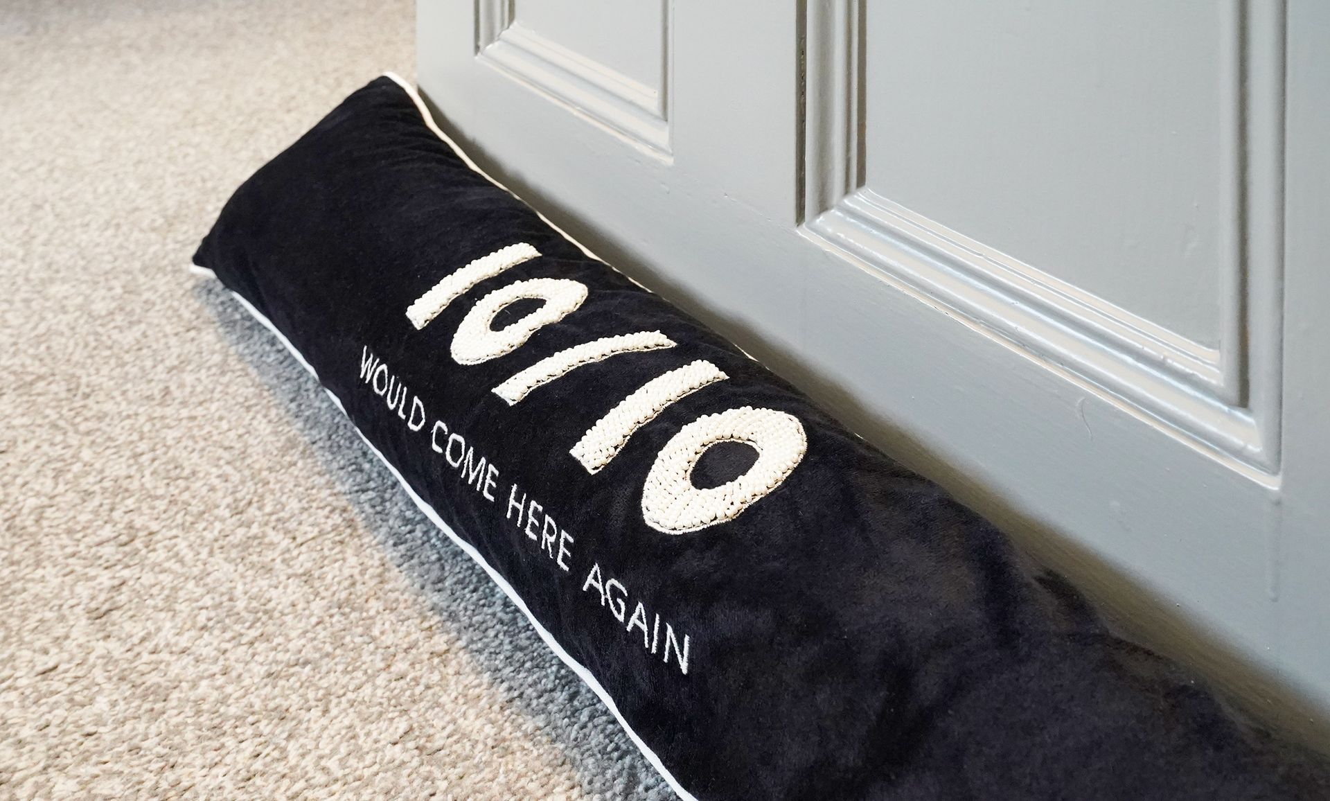 Black door draft stopper with white “10/10” text at the base of a painted door on carpet.