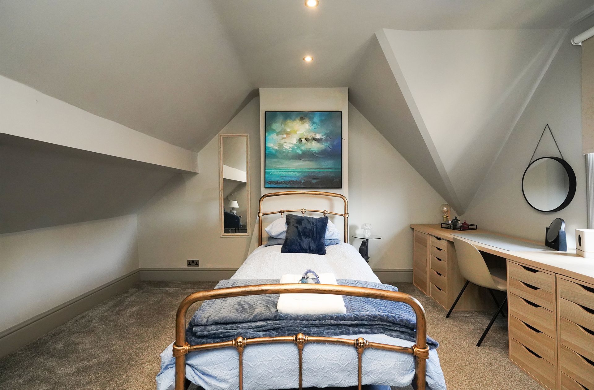 Cozy attic bedroom with twin bed, wooden desks, sloped ceiling, and ocean artwork above the bed