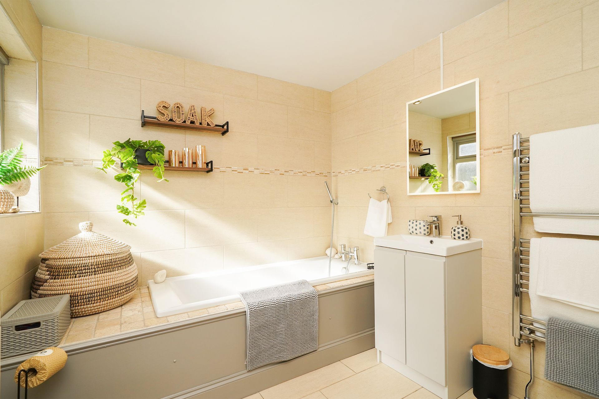 Bright beige bathroom with a bathtub, sink, mirror, plants, and woven decor