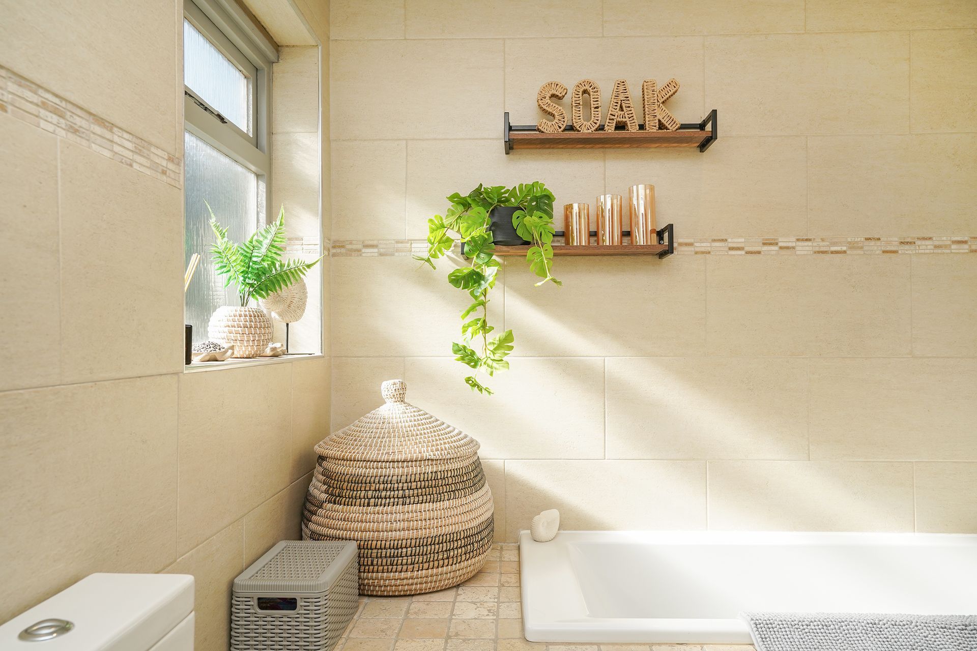 Bright beige bathroom with a bathtub, woven basket, shelves, and a plant by the window.