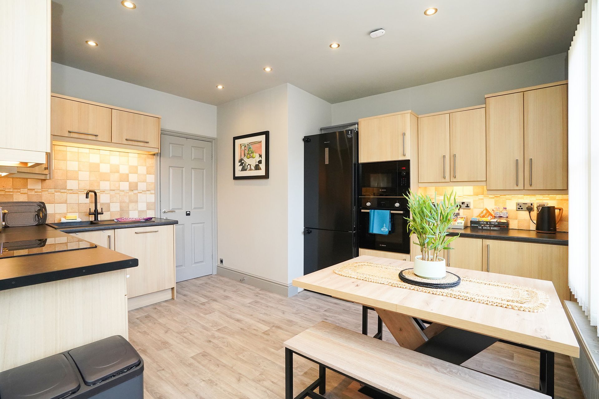 Bright modern kitchen with cream cabinets, black appliances, and a light wood dining table