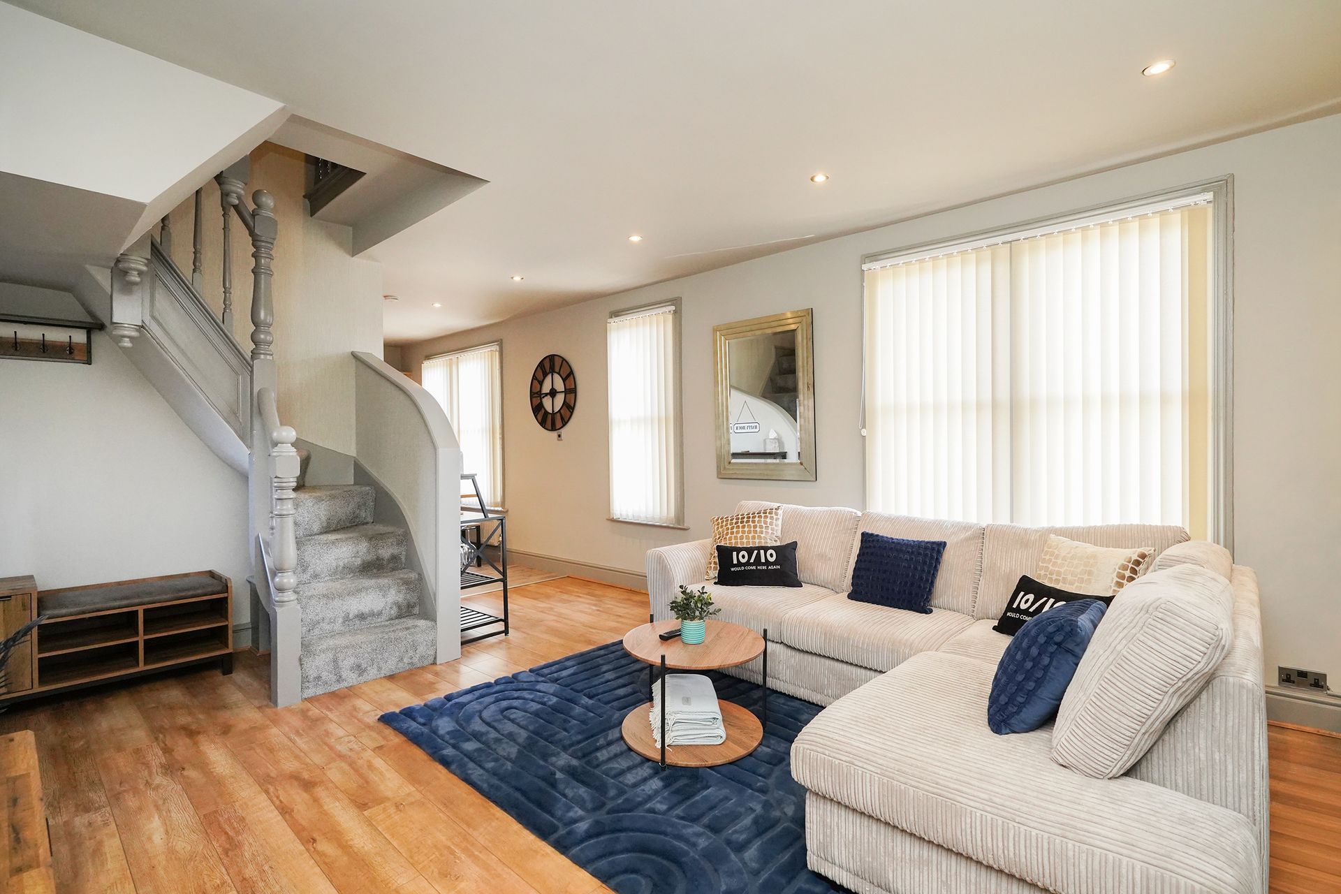 Bright living room with sectional sofa, blue rug, staircase, and hardwood floors