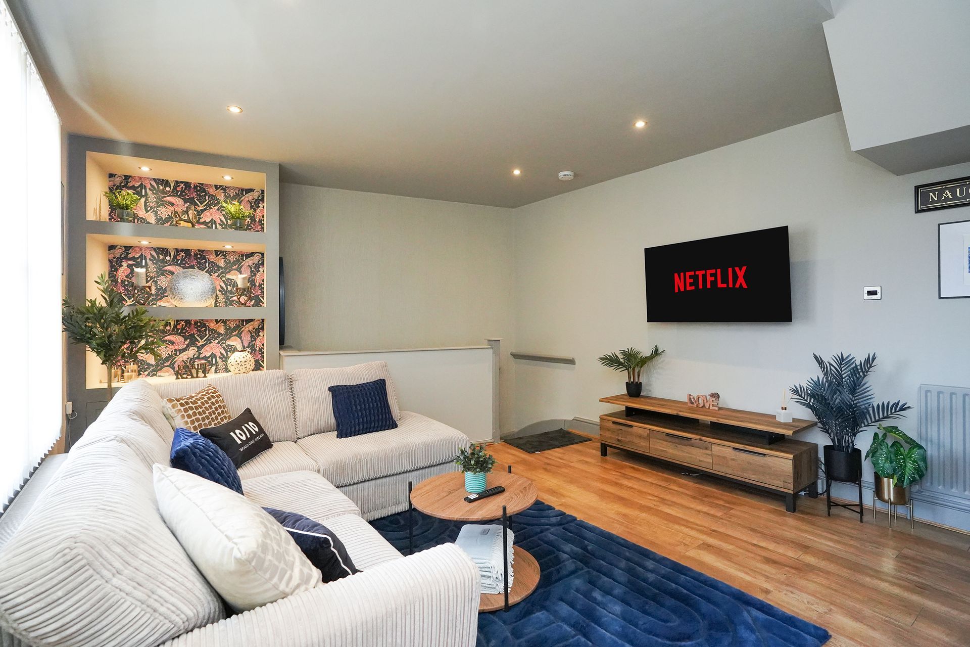 Cozy living room with white sofas, blue rug, wood floor, and wall-mounted TV showing Netflix