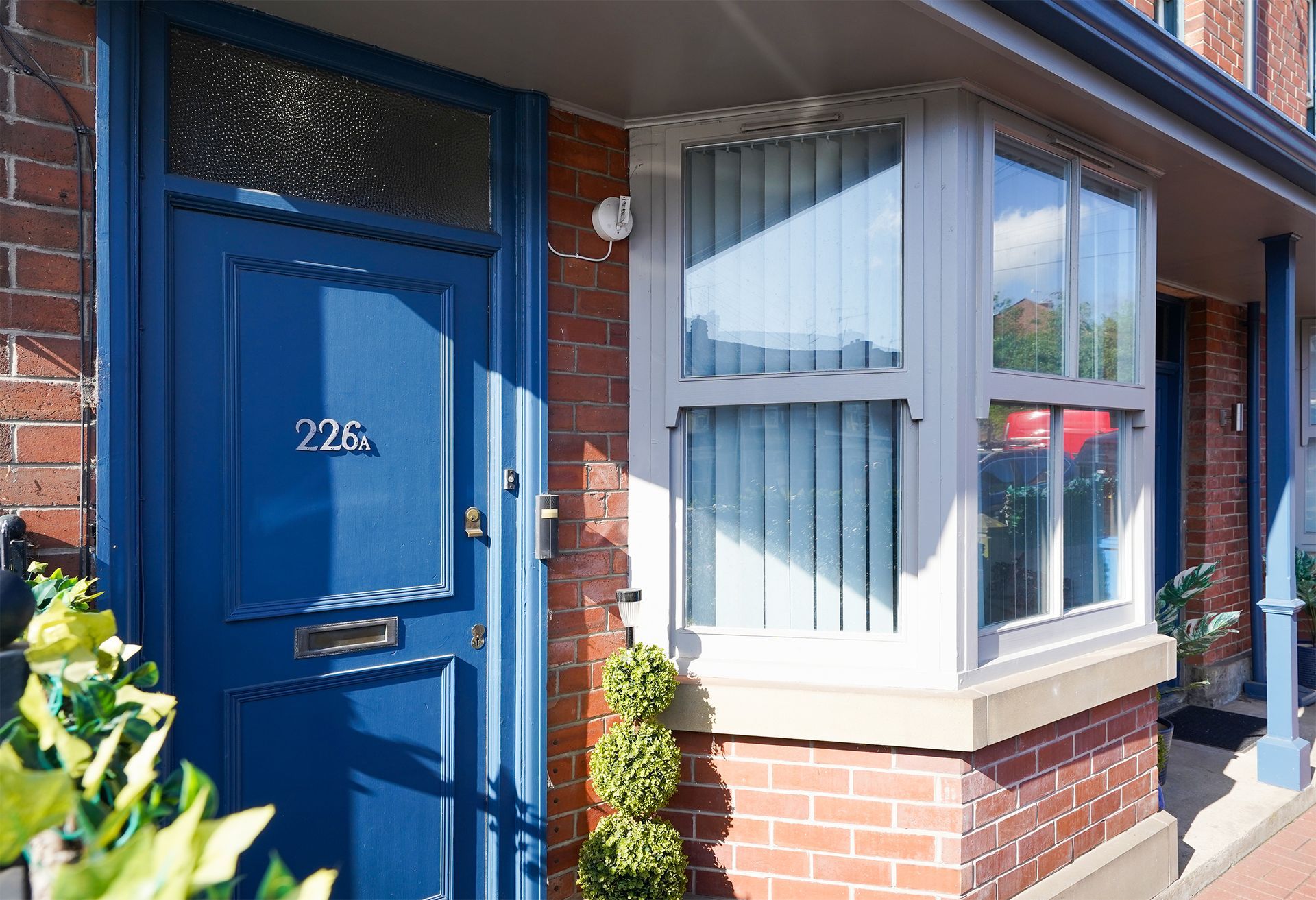 Blue front door beside a bay window on a brick house in sunlight