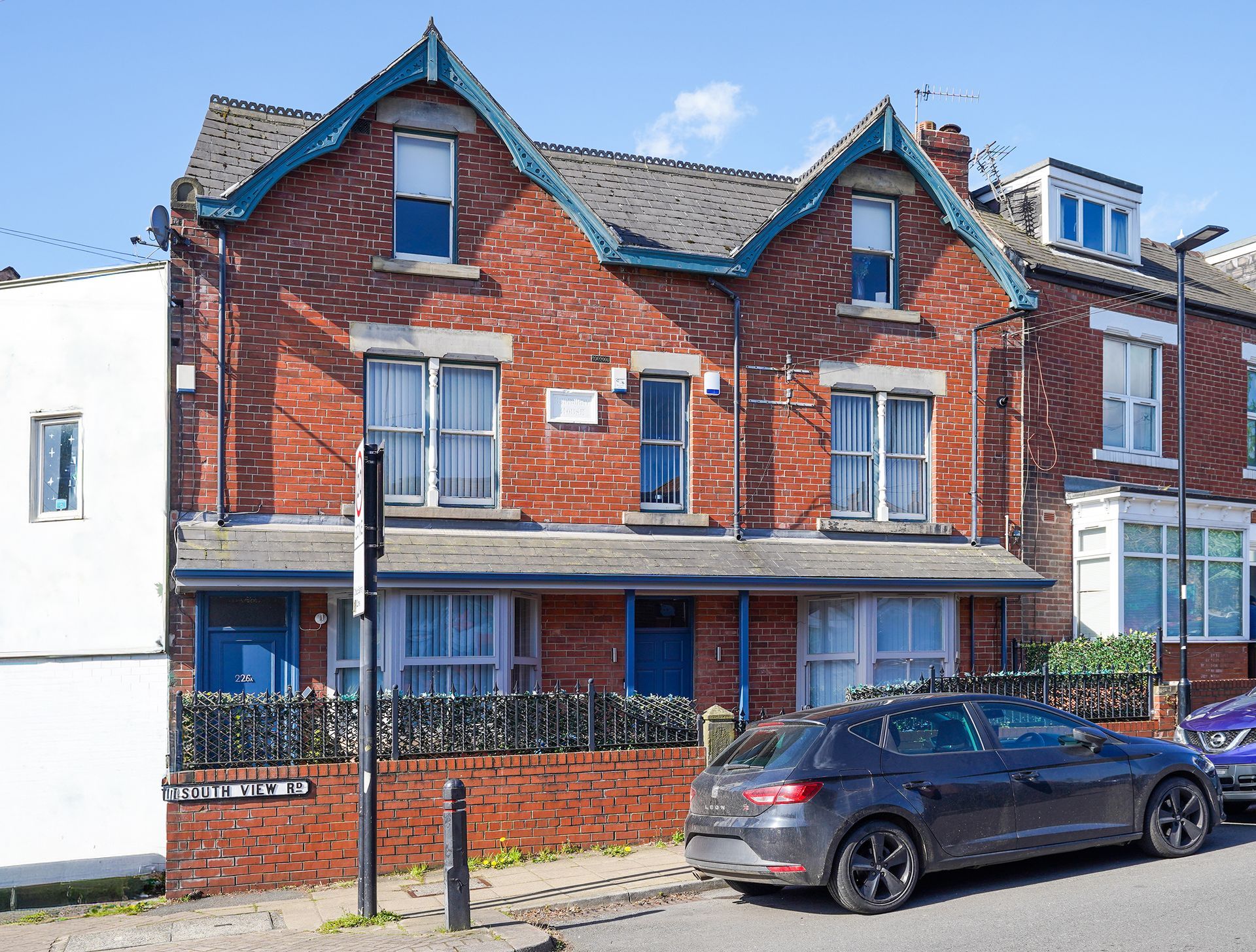 Red brick townhouse with white trim and a parked black car on a residential street.