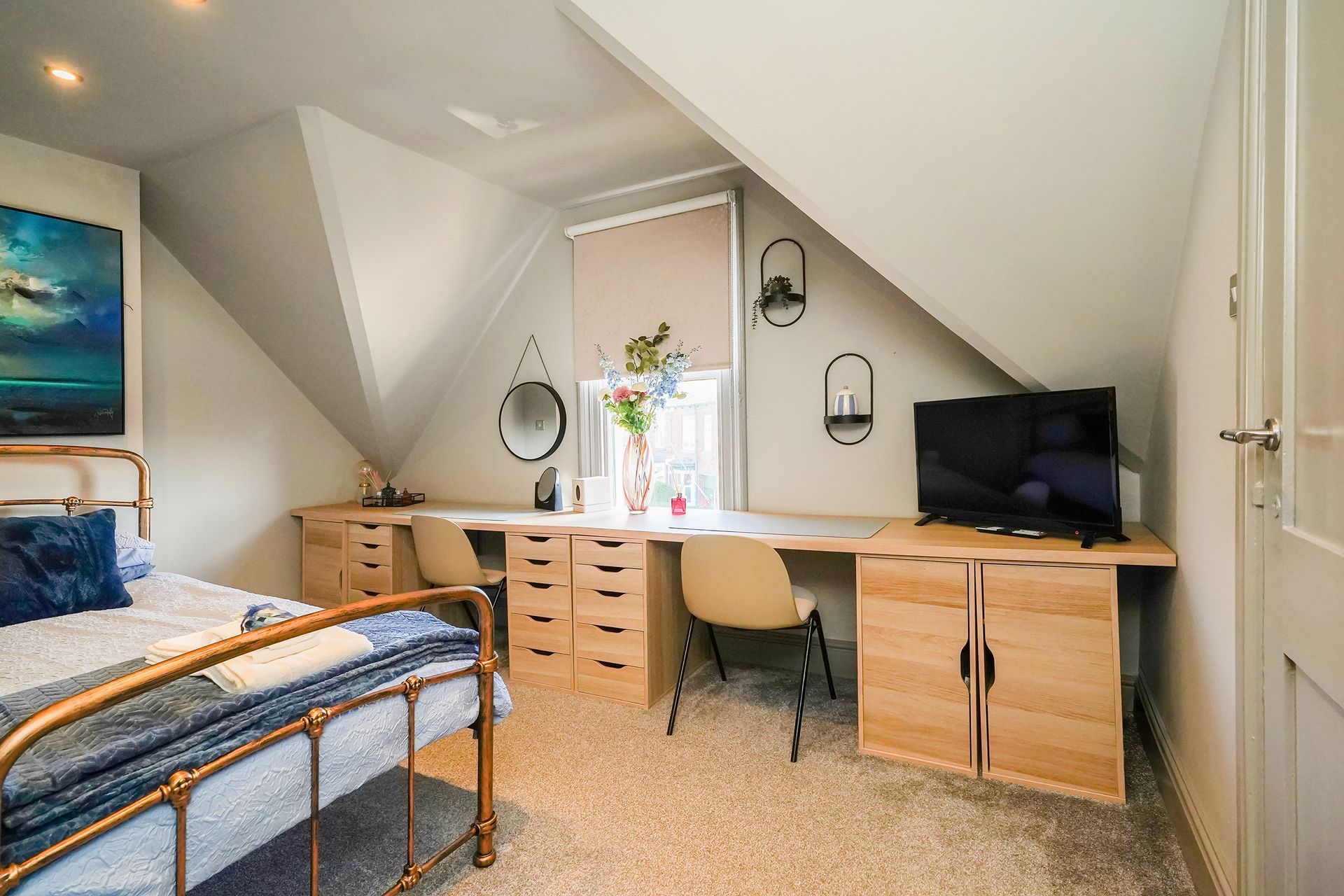 Attic bedroom with bed, desk, chair, drawers, and TV under sloped white ceiling