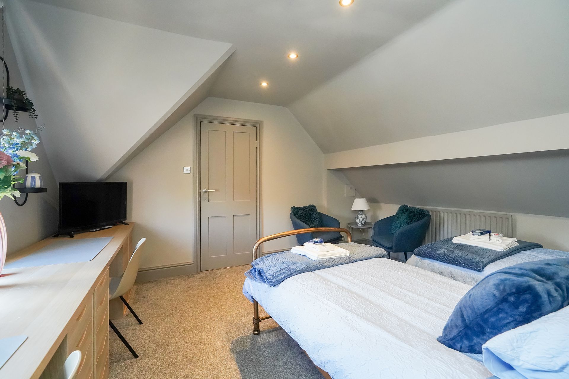 Small attic bedroom with twin beds, sloped ceiling, desk, and closet door.