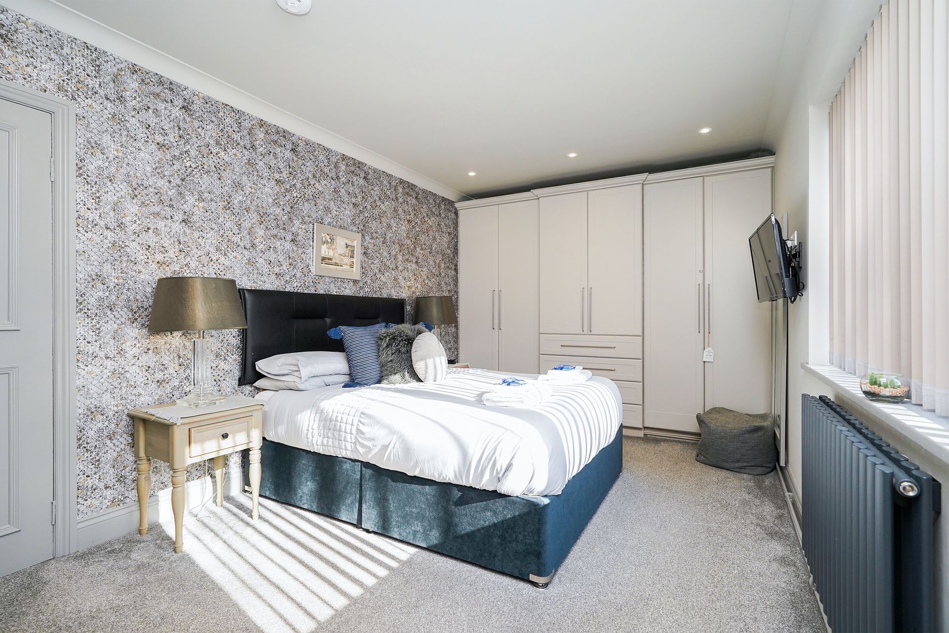 Bright modern bedroom with bed, wardrobe, patterned wallpaper, and large window with sheer curtains