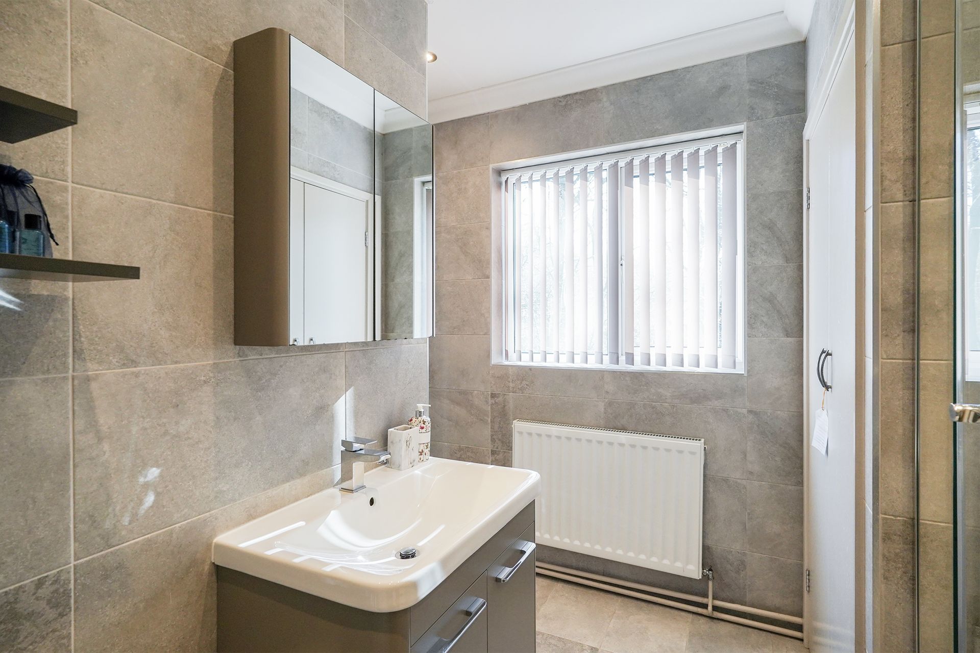 Modern bathroom with sink, mirror cabinet, tiled walls, shower, window, and radiator.