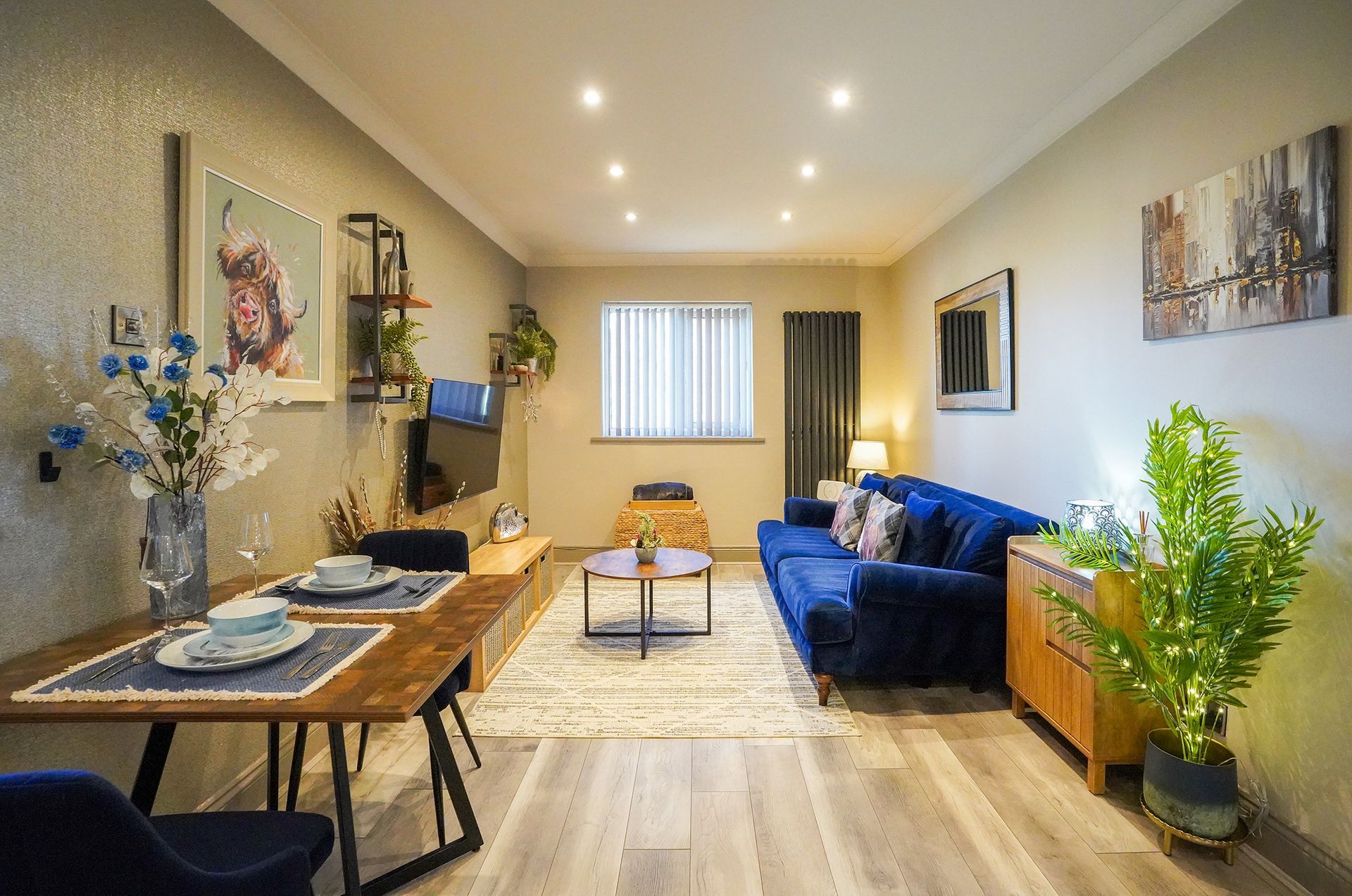 Bright living room with blue sofa, wooden table, potted plant, and wall art.