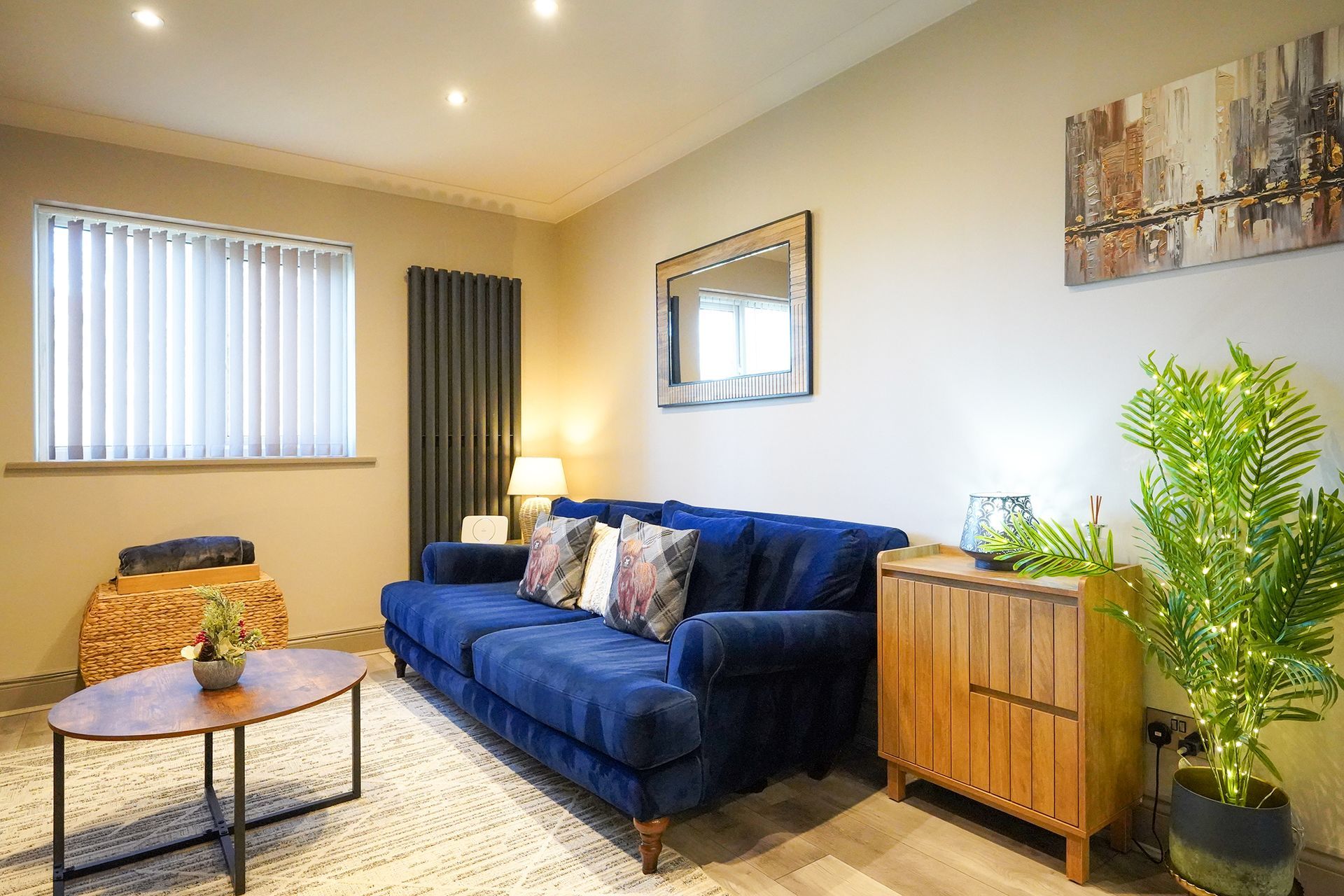 Bright living room with blue sofa, wooden cabinet, coffee table, mirror, and potted plant by a window.