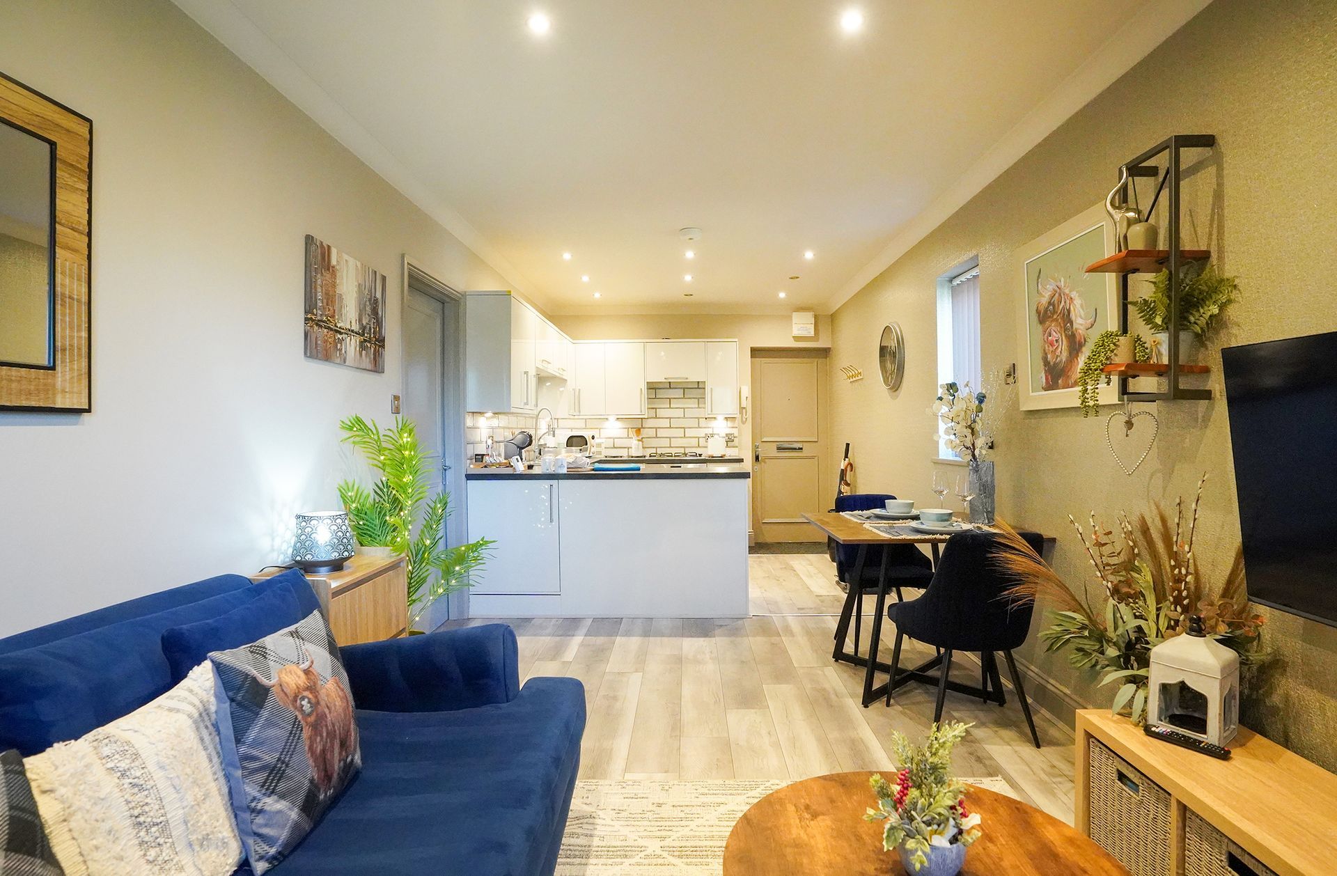 Cozy open-plan living room with blue sofa, dining table, and kitchen in the background