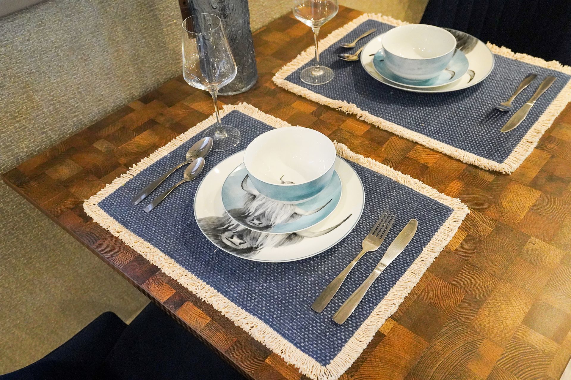 Two-place table setting with white cups on blue placemats over a rustic wooden table