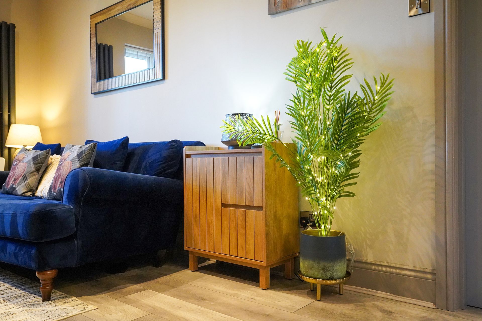 Living room with a blue sofa, wooden cabinet, wall mirror, and a tall potted plant