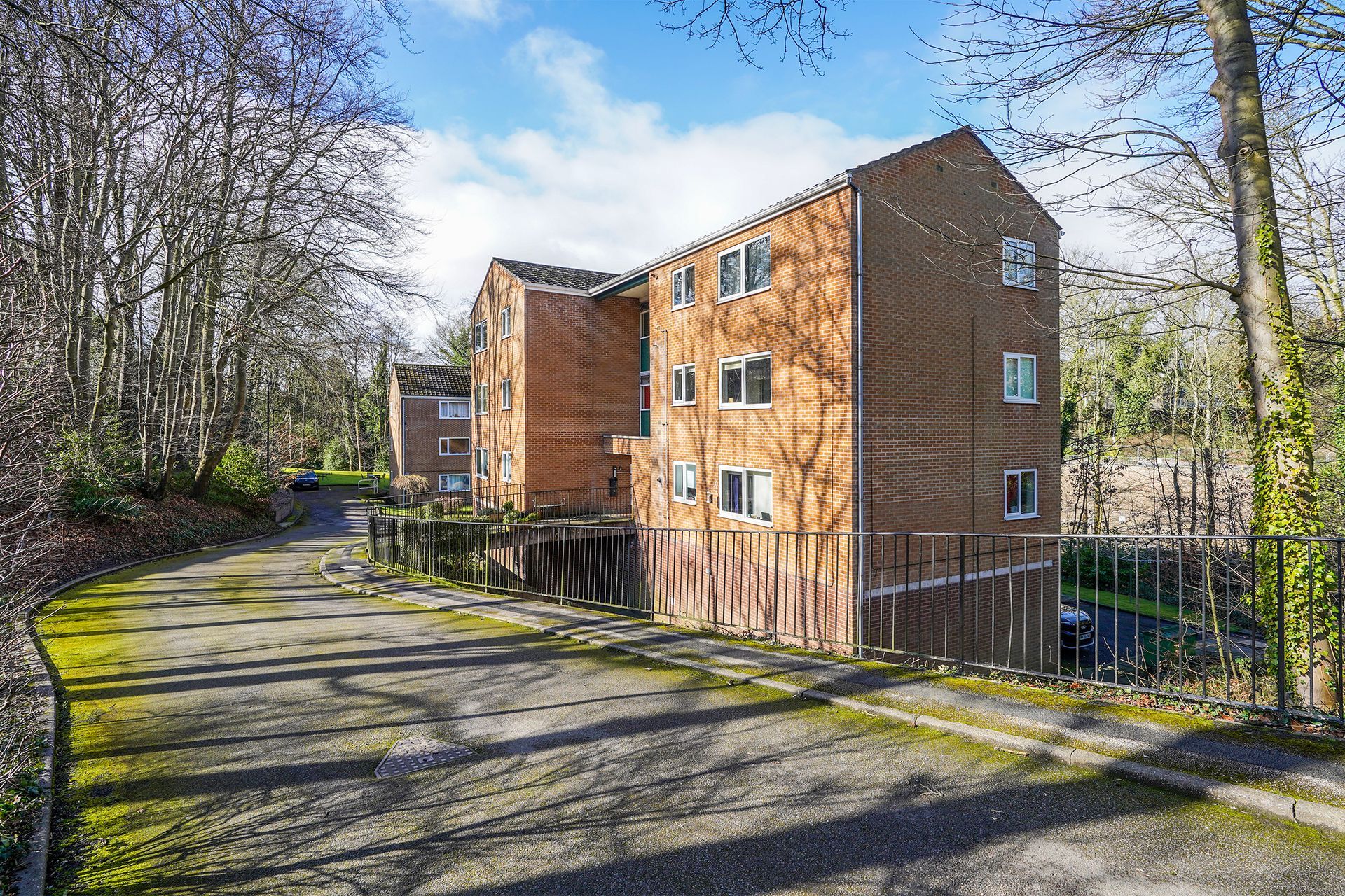 Modern brick apartment building beside a tree-lined road on a sunny day