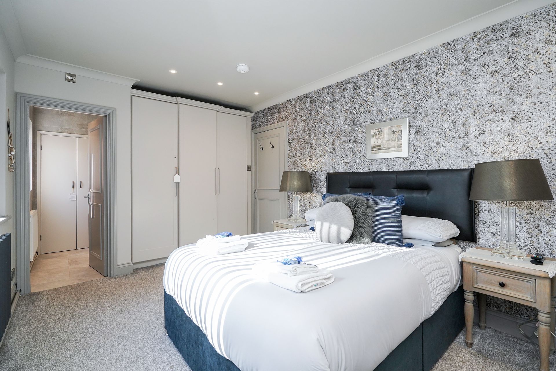 Bright modern bedroom with a large bed, floral wallpaper, wardrobe, and bedside lamps