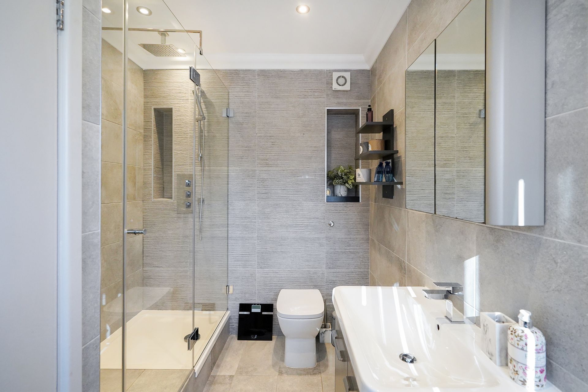 Modern bathroom with glass shower, toilet, sink, and gray tiled walls