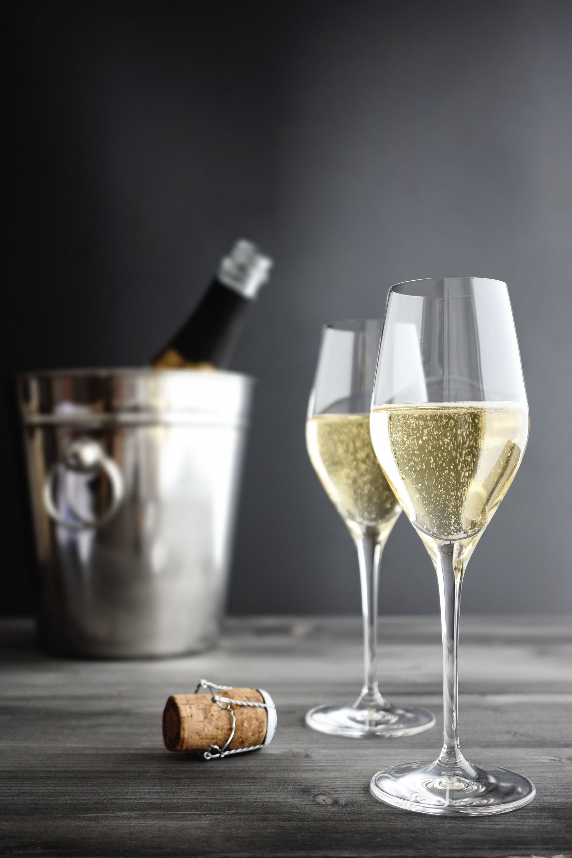 Two champagne flutes with sparkling wine beside a chilled bottle and cork on a table