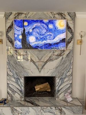 Wall-mounted TV showing Van Gogh’s Starry Night above a marble fireplace with a stone hearth.