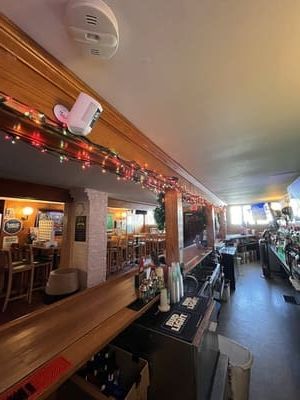 Cozy restaurant bar with wooden counters, holiday lights, and dining tables along a narrow aisle