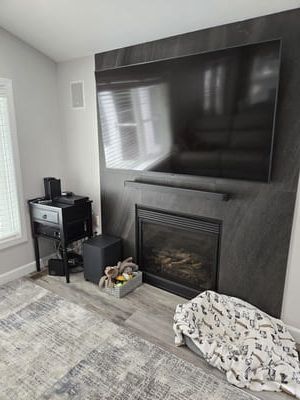 Modern living room with wall-mounted TV above a dark fireplace and light gray decor