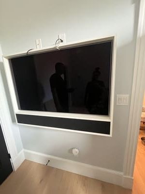Wall-mounted TV with a black soundbar or shelf beneath it on a white wall in a bright room