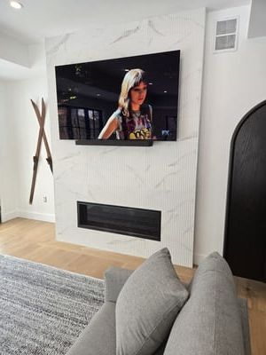 Modern living room with wall-mounted TV above a white fireplace and gray sofa in the foreground