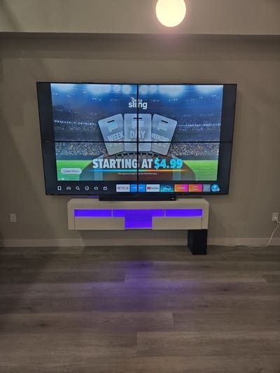 Wall-mounted TV showing a sports ad above a floating console with purple LED lighting in a modern room
