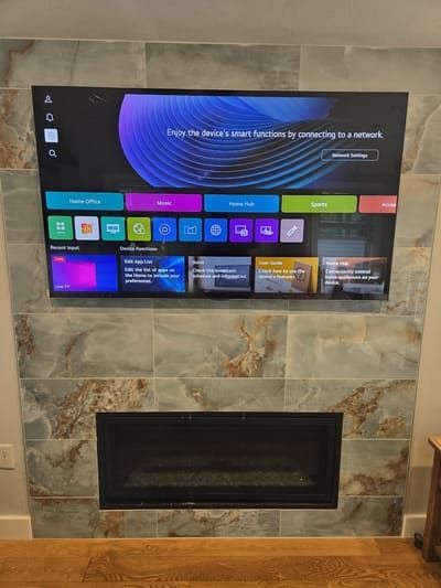 Wall-mounted TV above a black fireplace on a stone-tile wall in a living room