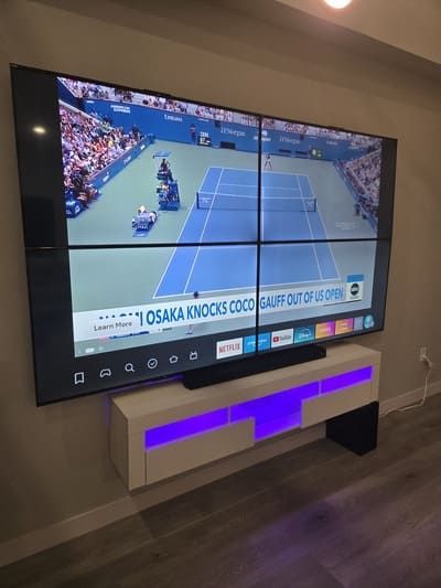 Wall-mounted TV showing a tennis match in a modern room with purple-lit cabinet below