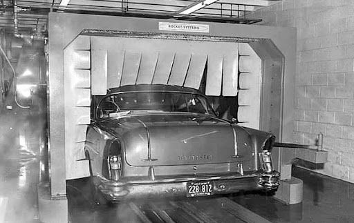 Classic car in a vintage car wash, being sprayed by water curtains.