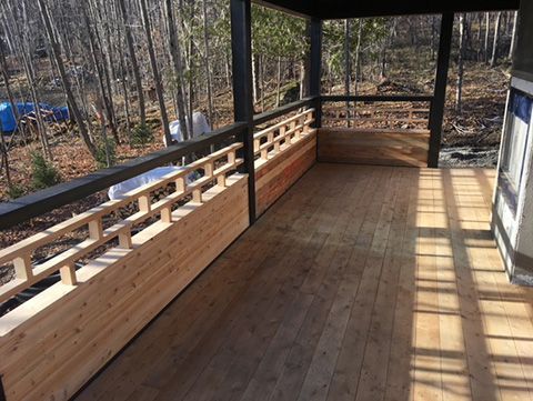 Porche en bois avec balustrade décorative, donnant sur une zone boisée.