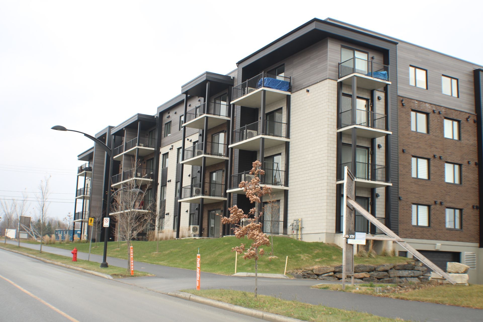 Immeuble d'appartements moderne à plusieurs étages avec balcons, situé à côté d'une rue avec une pelouse herbeuse.