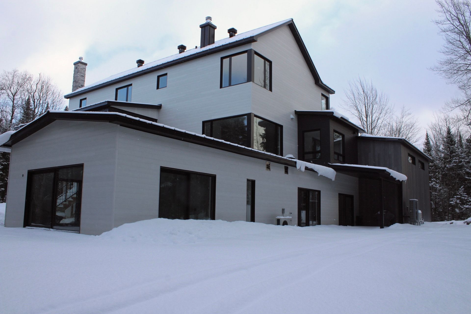 Maison blanche à deux étages avec des boiseries et des fenêtres sombres, recouverte de neige.