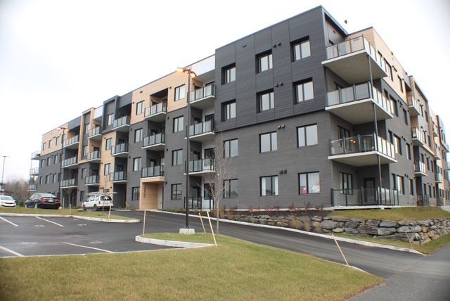 Immeuble d'appartements moderne avec façade gris foncé et beige, balcons et parking.