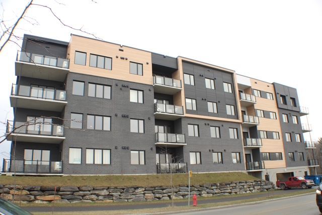 Immeuble d'appartements moderne à plusieurs étages avec extérieur noir et beige, balcons et parking.