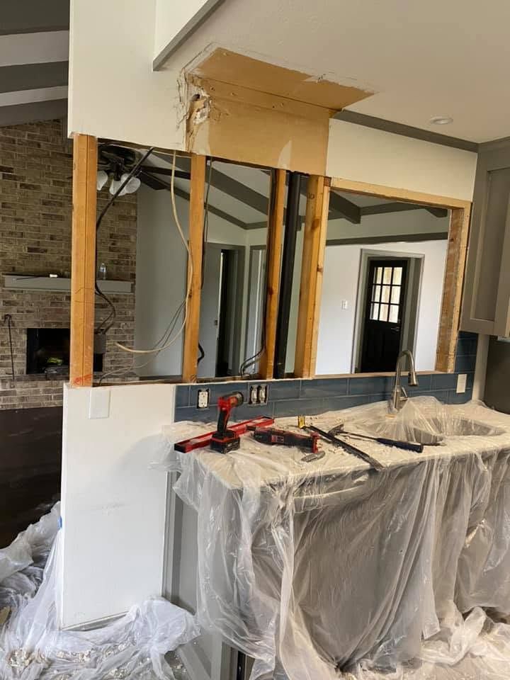 Home renovation site with partially demolished interior wall, exposed studs, and plastic-covered cabinets