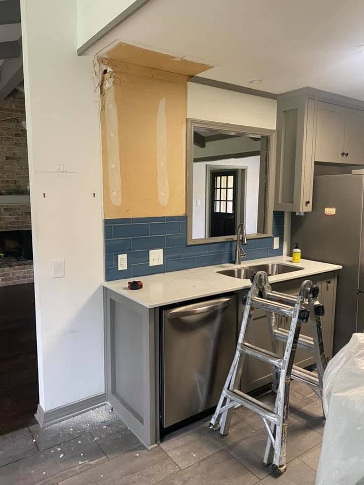 Kitchen renovation with open cabinets, blue backsplash, mini fridge, and step ladder nearby
