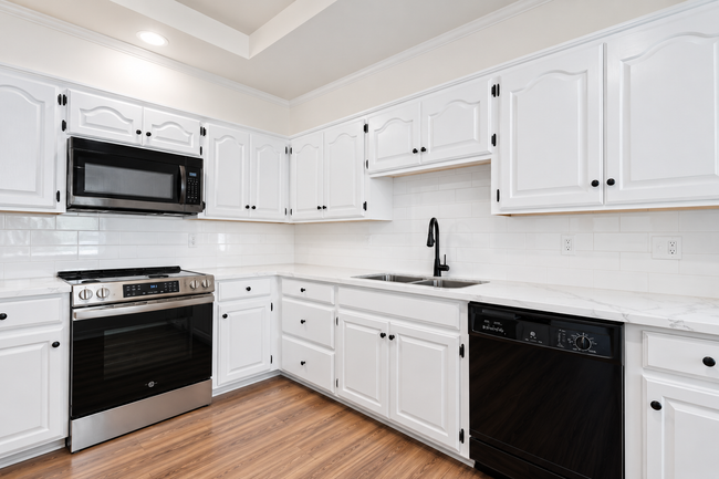 White kitchen with stainless steel appliances, black dishwasher, and light wood flooring