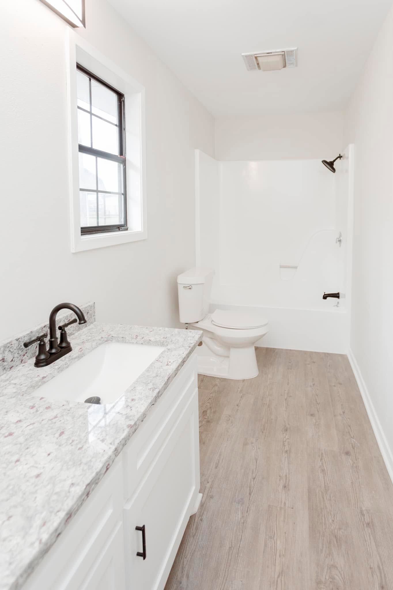 Bright white bathroom with marble vanity, toilet, black fixtures, and light wood floor