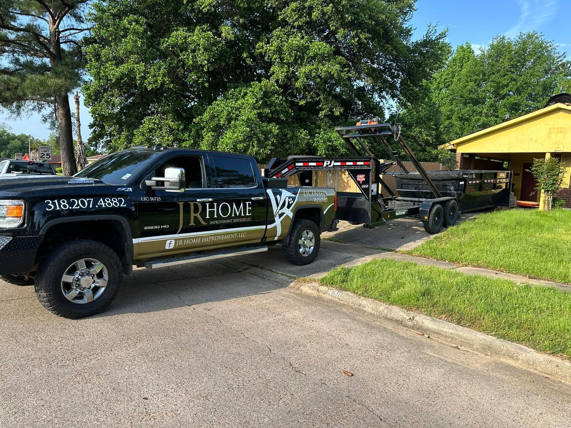 Black J. Rome towing truck hauling a trailer beside a yellow house on a sunny residential street