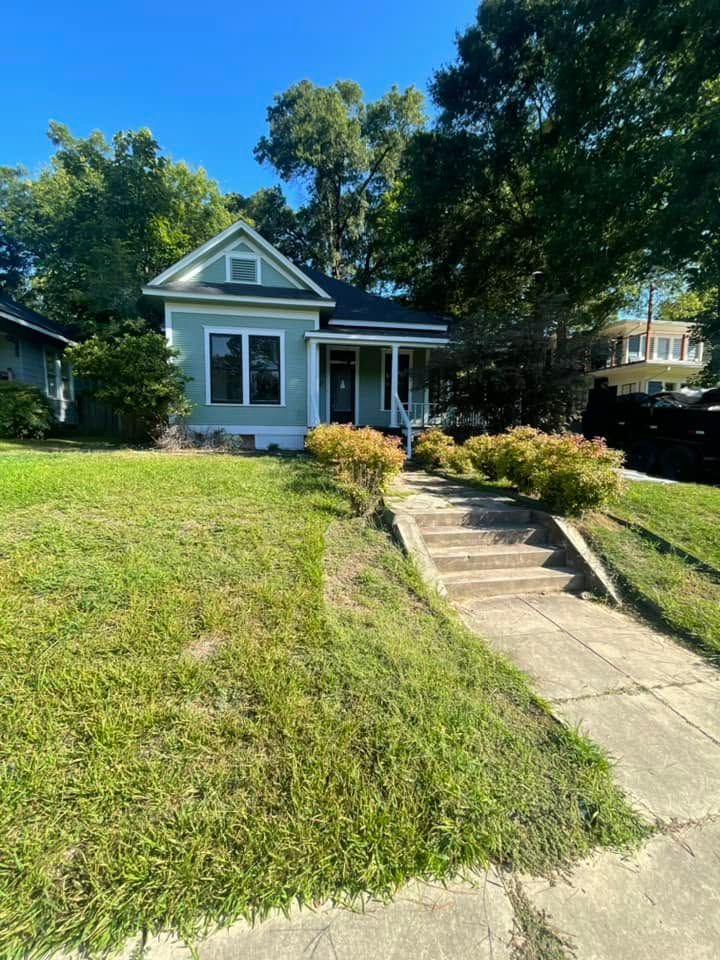 Small blue house with a front porch, walkway, and grassy yard on a sunny day