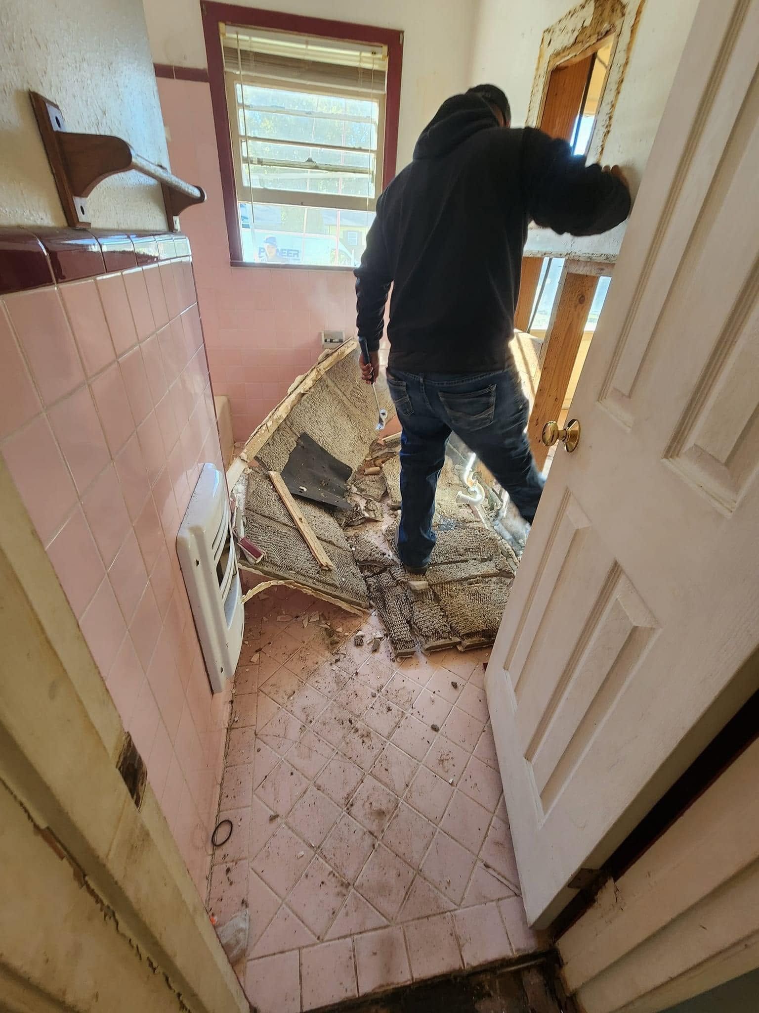 Person inspecting severe floor damage in a narrow hallway with broken tiles and debris.