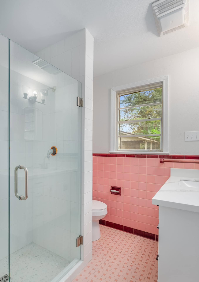 Pink-tiled bathroom with glass shower, white sink, and window above a toilet