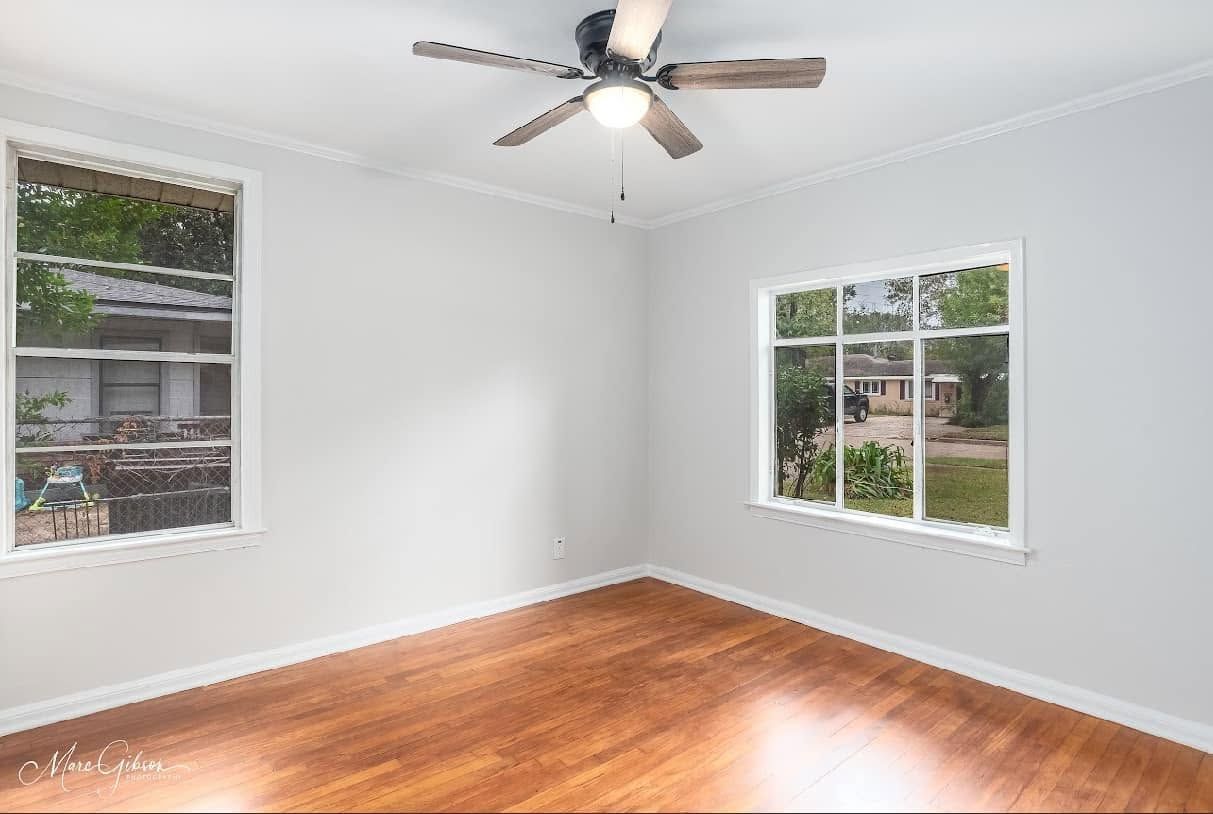 Empty white room with hardwood floor, two windows, and a ceiling fan.